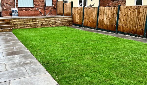 New artificial grass lawn in front of a timber fence