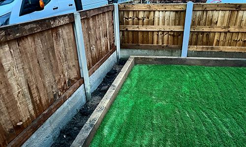 Artificial grass lawn edged with timber sleepers beside a new fence