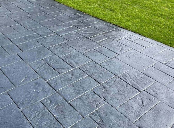 Grey pattern imprinted concrete in a slate design beside a lawn