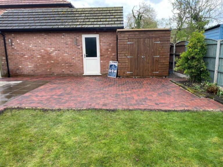 Red block paved patio by a garage with a new lawn