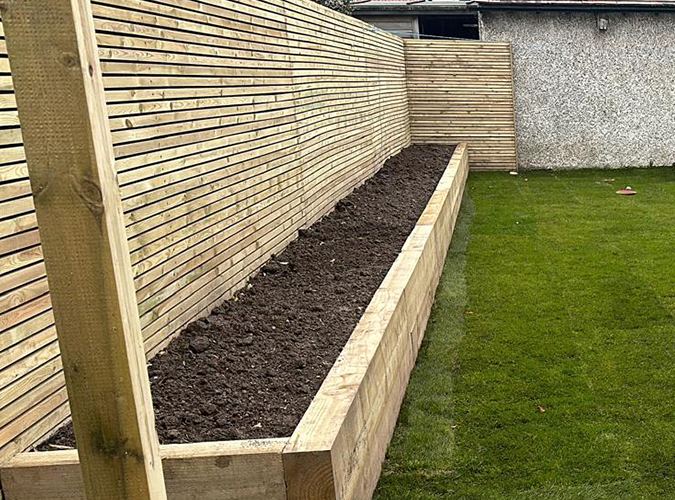 Slatted fence with a sleeper planter and a new lawn